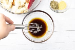hand with whisk, small bowl with oil and vinegar.