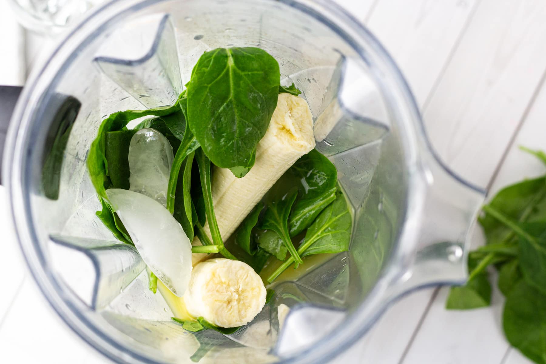 spinach, bananas, ice cubes and orange juice in blender