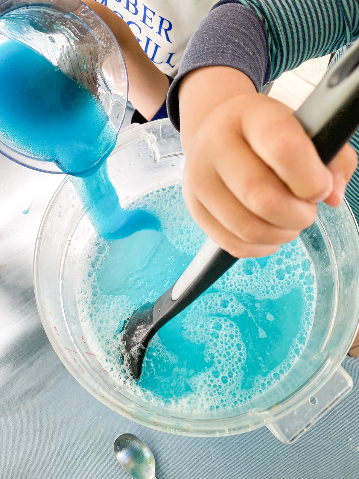 hands adding dish soap to water and stirring with big spoon.
