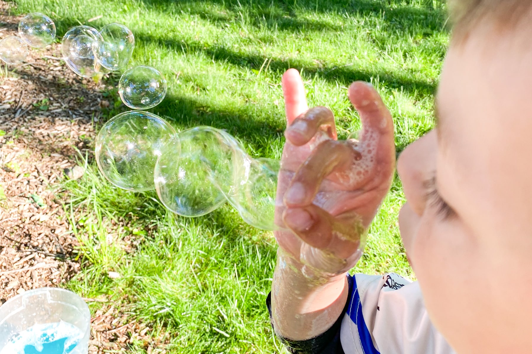 boy holding thumb and index finger together in ok sign and blowing bubbles through it.