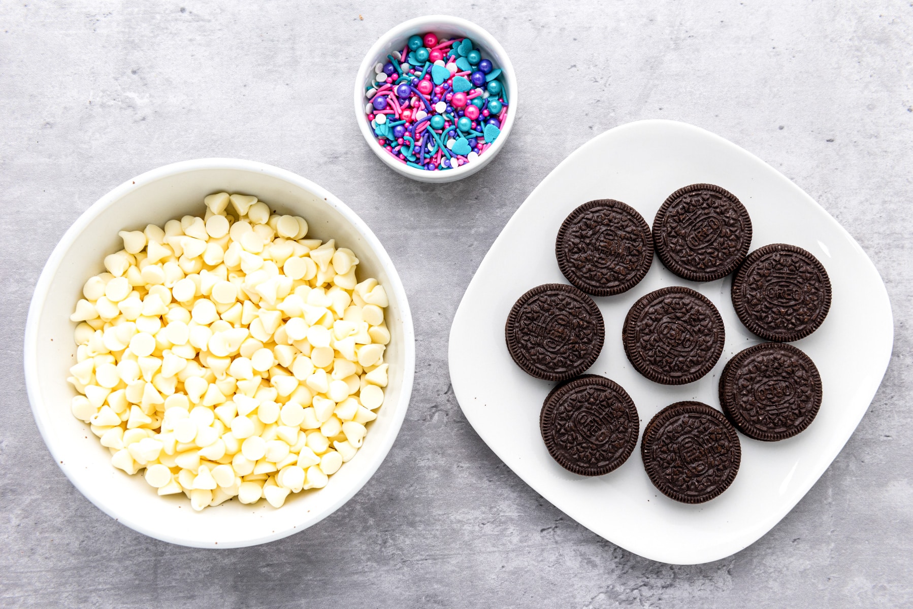 oreos, white chocolate chips and sprinkles in bowls.