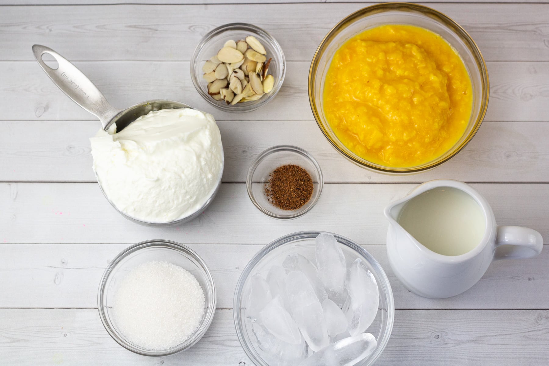 mango pulp, yogurt, milk, sugar, almonds, cardamon powder in bowls.